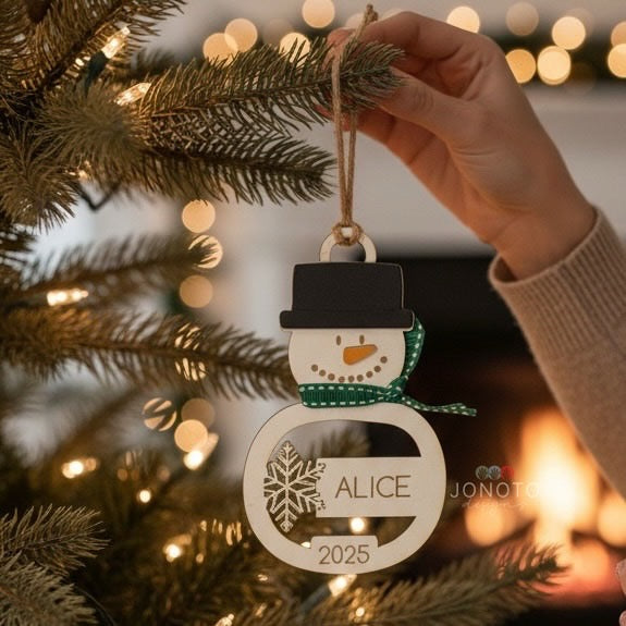 Hand hanging a personalized snowman ornament with 'ALICE' and '2025' on a decorated Christmas tree.