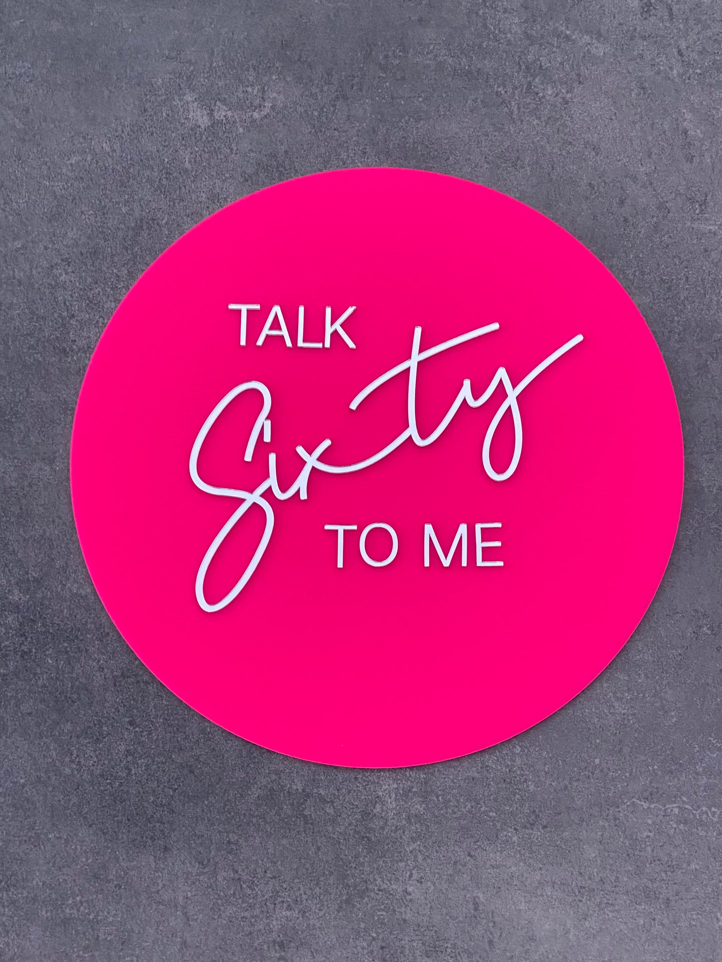 Bright pink circle acrylic sign with silver mirror writing saying Talk Sixty To Me - 60th Birthday sign